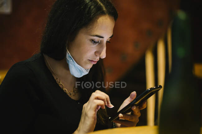 Woman wearing a mask using a mobile phone in a restaurant — Stock Photo