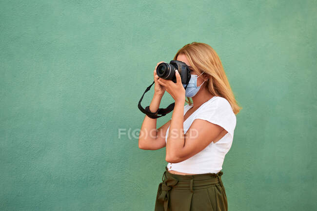 Junge Frau mit Maske und Kamera auf grünem Hintergrund — Stockfoto