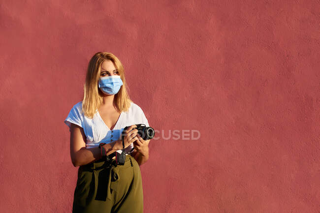 Молода жінка з маскою і фотоапаратом на червоному тлі — стокове фото