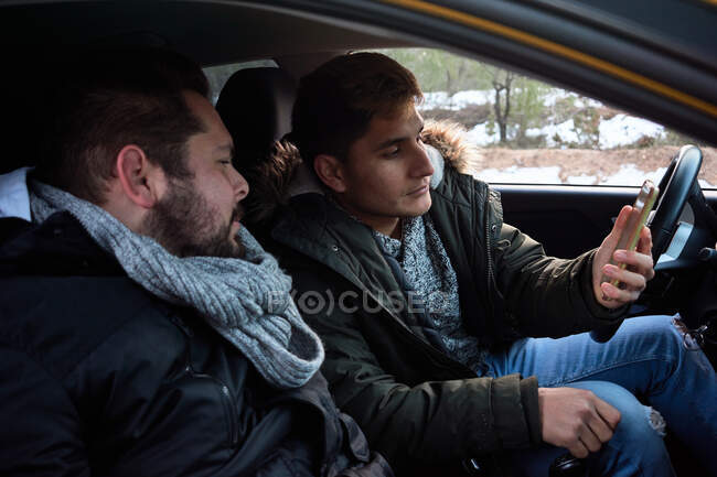 Dos jóvenes miran un teléfono dentro de un coche. Concepto de búsqueda de rutas - foto de stock