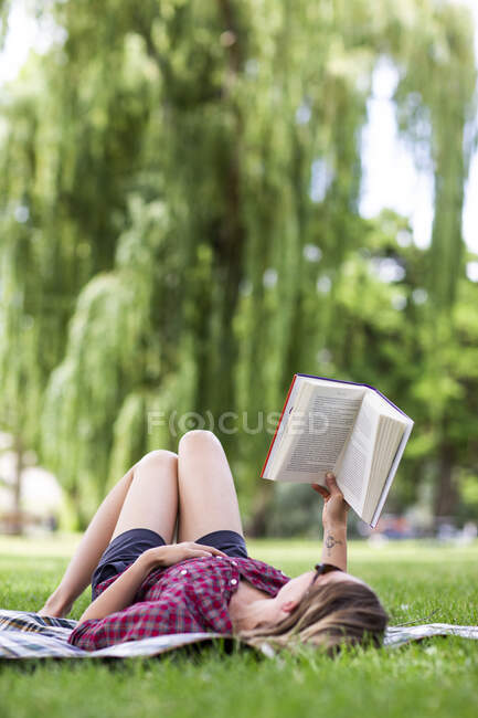 A young girl reads a book on her back in a park in the Columbia Gorge — Stock Photo