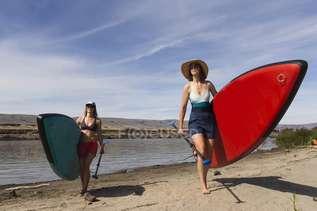 Zwei Frauen tragen ihre SUPs vom Columbia River in Oregon. — Stockfoto