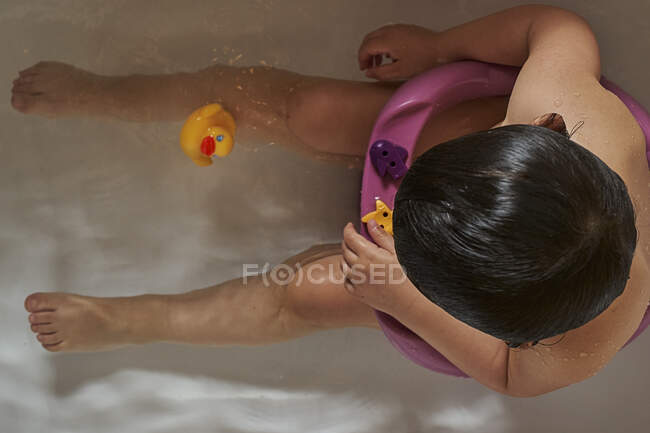 Bambino felice che gioca con schiuma di sapone nel bagno di casa. Anatra di gomma in bagno di schiuma. Igiene per bambini — Foto stock