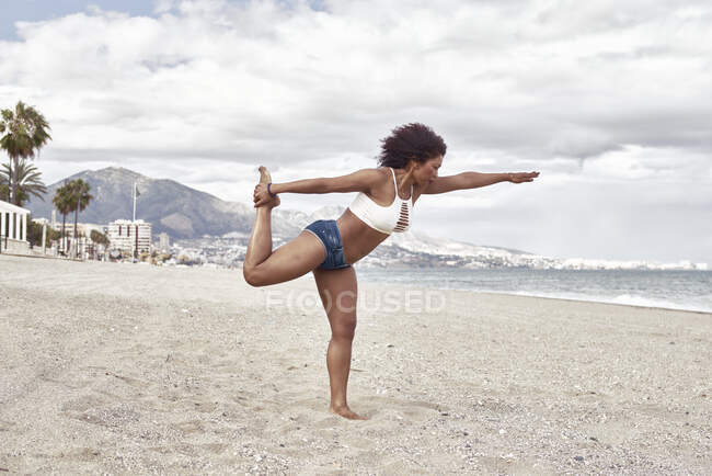 Mujer negra en jeans cortos posa en la playa equilibrando - foto de stock