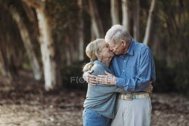 Porträt eines erwachsenen Rentnerehepaares, das sich im Wald küsst — Stockfoto