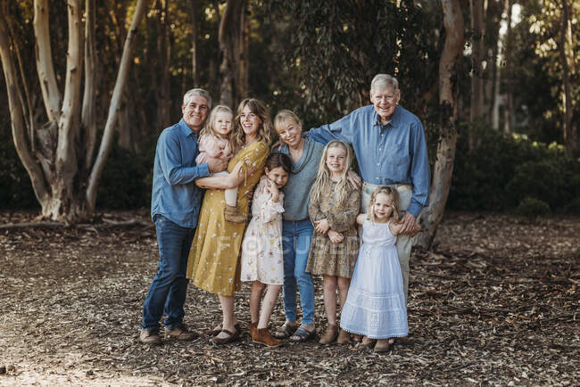 Retrato de una gran familia extendida sonriente abrazándose afuera en el bosque - foto de stock