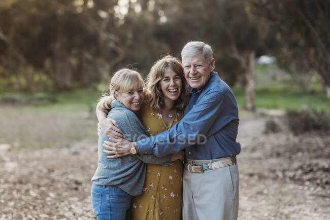 Retrato de una mujer adulta y padres mayores abrazándose en el parque - foto de stock