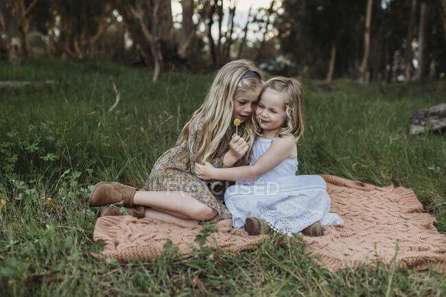 Две блондинки, сидящие на одеяле в поле с леденцами — стоковое фото