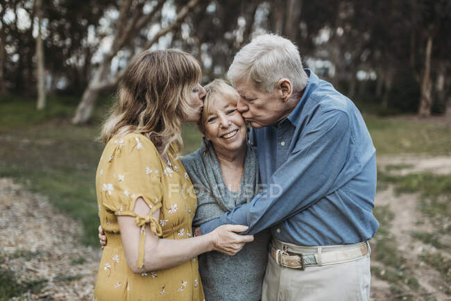 Mãe sênior sendo beijada pelo marido e filha adulta — Fotografia de Stock