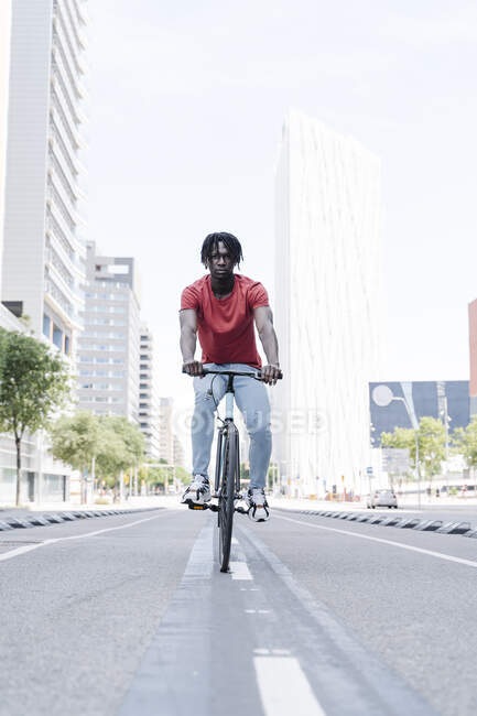 Vista laterale del ciclista afroamericano di sesso maschile in sella alla bicicletta sul terrapieno soleggiato — Foto stock