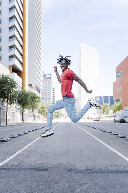 Side view of happy energetic black male jumping over road in summer city — Stock Photo