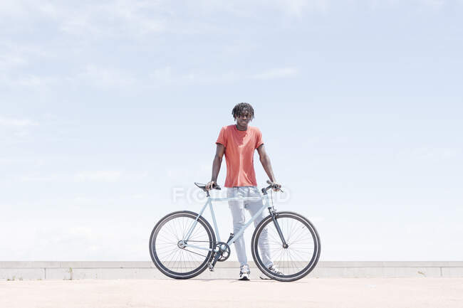 Fröhlicher Hipster Afroamerikaner mit Fahrrad steht bei sonnigem Wetter auf der Straße — Stockfoto