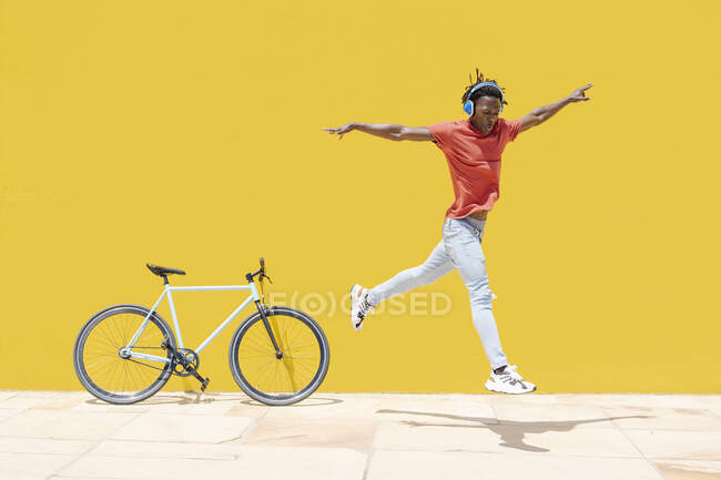 Чорний юнак стрибав під час танців на вулиці біля велосипеда і жовтої стіни. — стокове фото