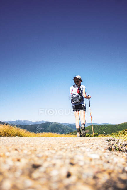 Femme randonnée sur route contre paysage de montagne et ciel bleu — Photo de stock