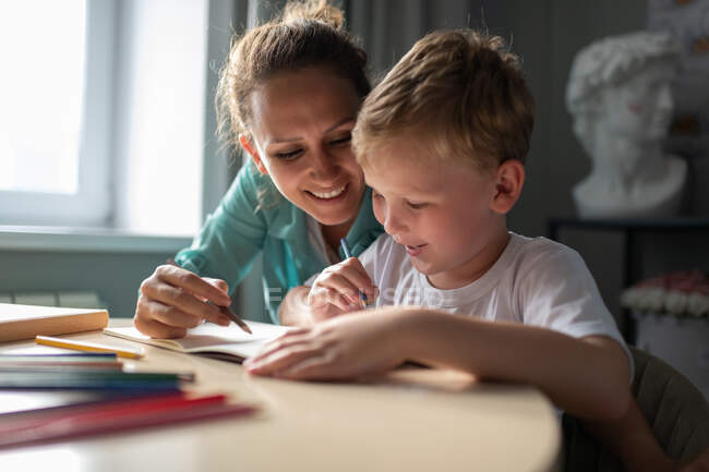 Glückliche erwachsene Mutter lächelt und zeichnet Bild mit Sohn am Wochenende zu Hause — Stockfoto