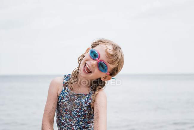 Jovencita riendo con sus gafas puestas mientras juega en la playa - foto de stock