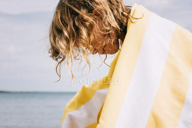Junges Mädchen mit lockigem Haar, am Strand in ein gestreiftes Handtuch gehüllt — Stockfoto