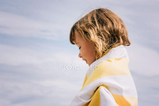 Chica sonriendo envuelta en una toalla a rayas en la playa - foto de stock