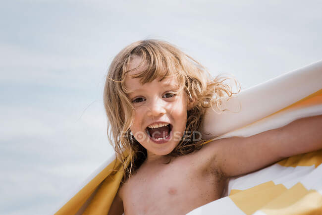 Mädchen lacht, während sie am Strand in ein gestreiftes Handtuch gehüllt ist — Stockfoto