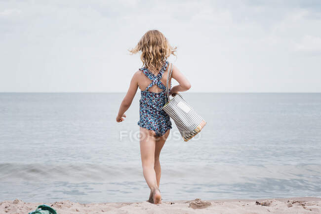Young girl holding a beach bag strutting towards the sea — Stock Photo