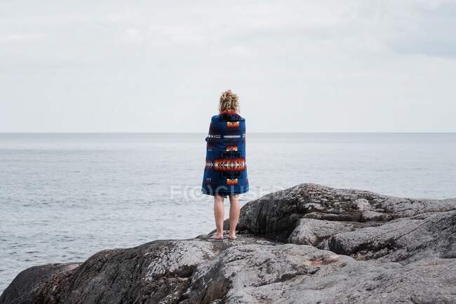 Donna in piedi su rocce avvolta in una coperta di Pendleton in Svezia — Foto stock