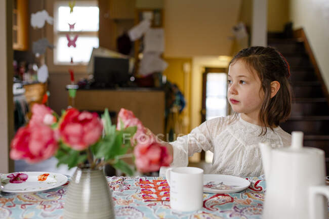 A small child in a lace dress sits alone at a table set for tea party — Stock Photo