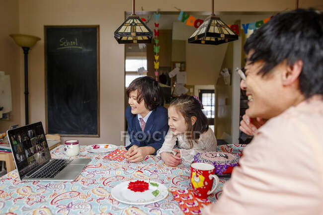 A smiling family sits at table on a zoom meeting birthday party — Stock Photo