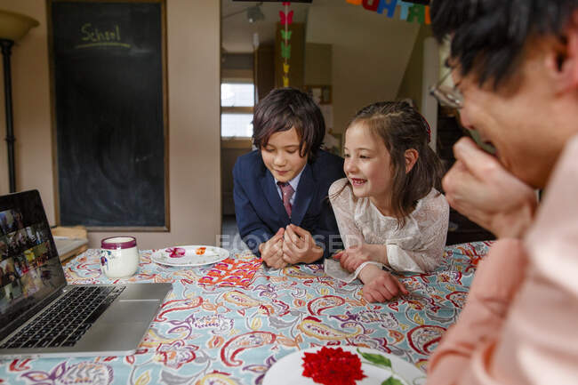 Smiling girl in fancy dress sits with family at table on zoom meeting — Stock Photo