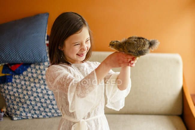 Joyful child holding a small fluffy baby chicken aloft in her hand — Stock Photo