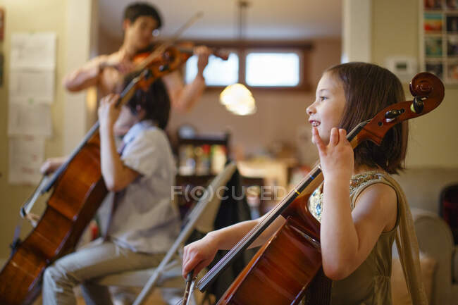 A happy child plays cello with family in background playing music — Stock Photo
