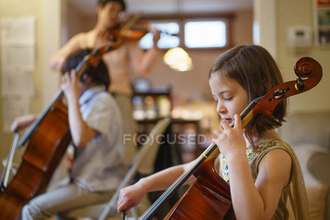 A small child plays cello concert with her family in the living room — Stock Photo
