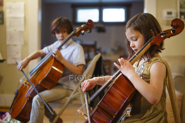 A brother and sister practice cello together in their living room — Stock Photo