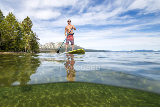 Un hombre de pie paddle boarding en Lake Tahoe, CA - foto de stock