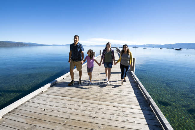 Семья улыбается и держится за руки, спускаясь по пирсу в солнечный день в Саут Лейк Тахо, Калифорния. — стоковое фото