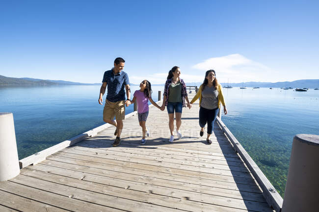 Uma família sorri e segura as mãos andando por um cais em um dia ensolarado em South Lake Tahoe, Califórnia. — Fotografia de Stock