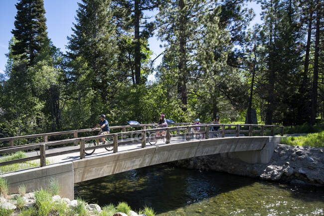 Uma família cruza uma ponte sobre Taylor Creek em bicicletas em um belo dia de verão perto de South Lake Tahoe, Califórnia. — Fotografia de Stock