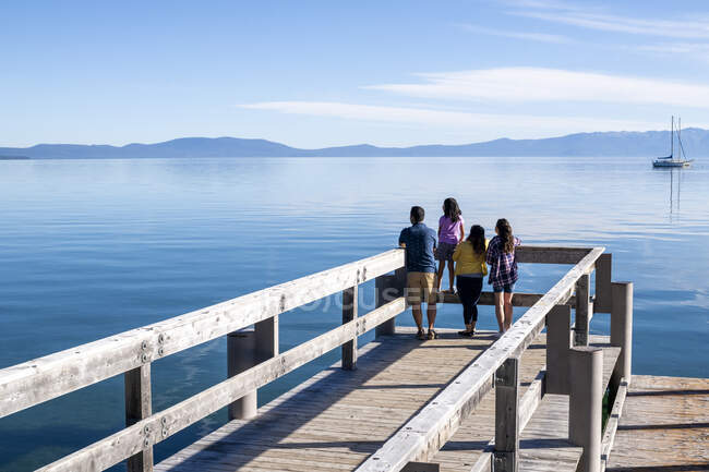 Una familia contempla las tranquilas aguas del lago Tahoe desde un muelle en un soleado día de verano en South Lake Tahoe, California. - foto de stock