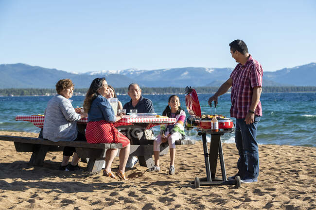 Une famille multigénérationnelle profite d'un barbecue sur une plage du lac Tahoe, Nevada. — Photo de stock