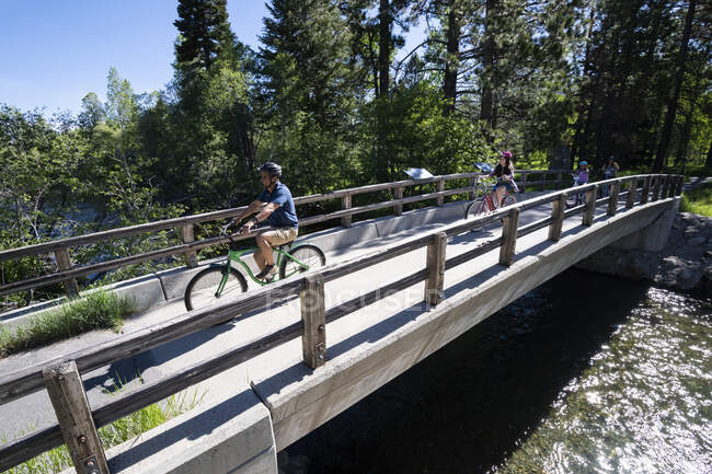 A family crosses a bridge over Taylor Creek on bikes on a beautiful summer day near South Lake Tahoe, California. — Stock Photo