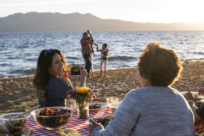 Una madre toma una foto de su esposo y sus hijos jugando en la costa de Nevada Beach durante el atardecer en Lake Tahoe, Nevada. - foto de stock