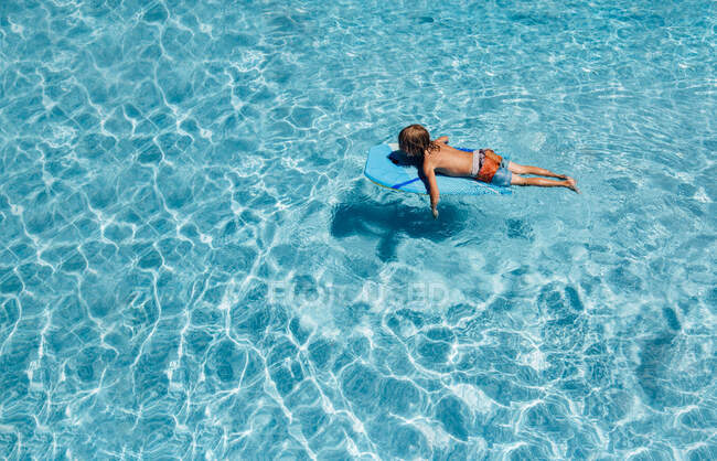 Jeune garçon flottant dans la piscine un jour d'été — Photo de stock