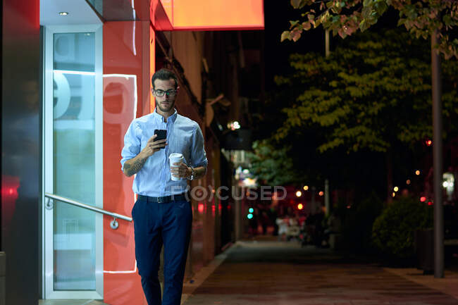 Joven hombre de negocios camina con su teléfono inteligente y taza de café - foto de stock