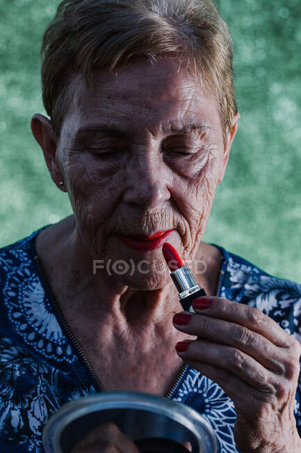 Anciana pintándose los labios de rojo mirándose en el espejo - foto de stock