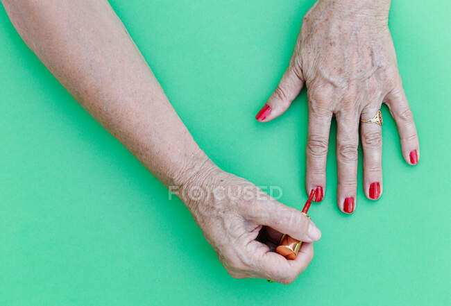 Les personnes âgées peignent ses ongles en rouge avec un fond vert, plat sur le dessus — Photo de stock