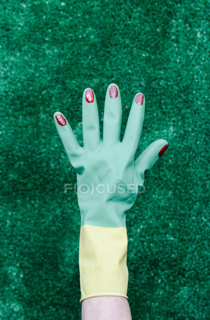 Mano con guante de plástico y uñas pintadas de rojo sobre fondo verde - foto de stock