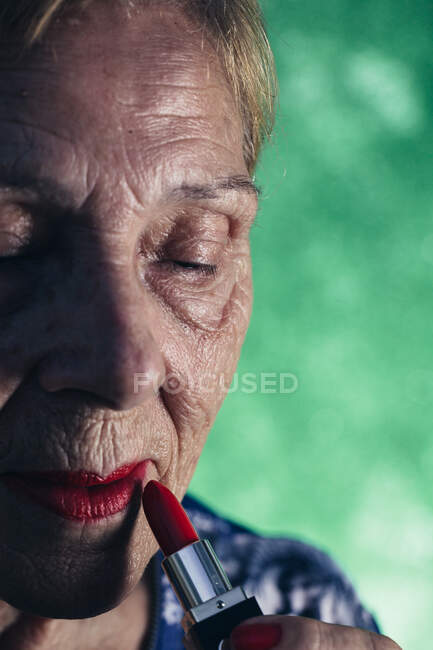 Mulher velha em primeiro plano vestindo batom vermelho em um fundo verde — Fotografia de Stock