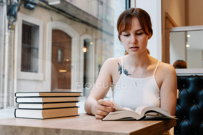 Jovem mulher sentada em um refeitório lendo livros — Fotografia de Stock