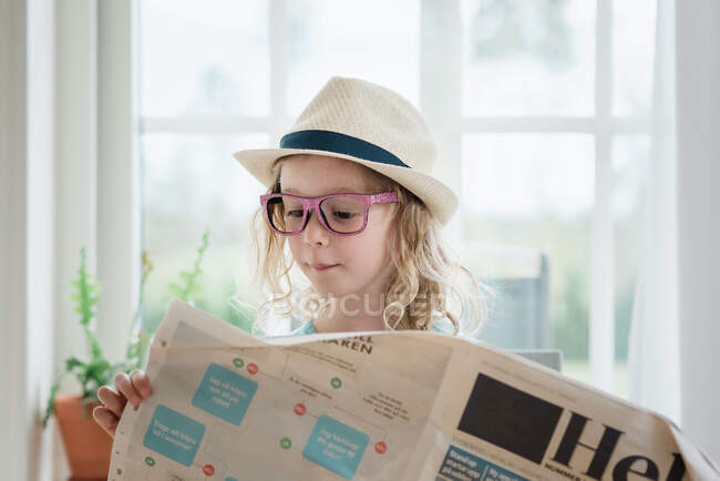 Young girl reading a newspaper with a hat and glasses on — Stock Photo