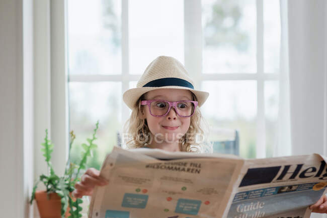 Young girl pulling funny faces whilst reading a newspaper — Stock Photo