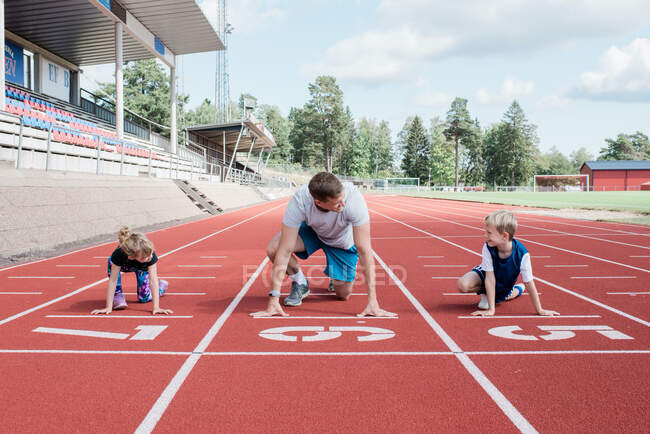 Father and his kids getting ready to run on a track to race — Stock Photo